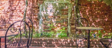 A brick wall with a metal table and two chairs in front.