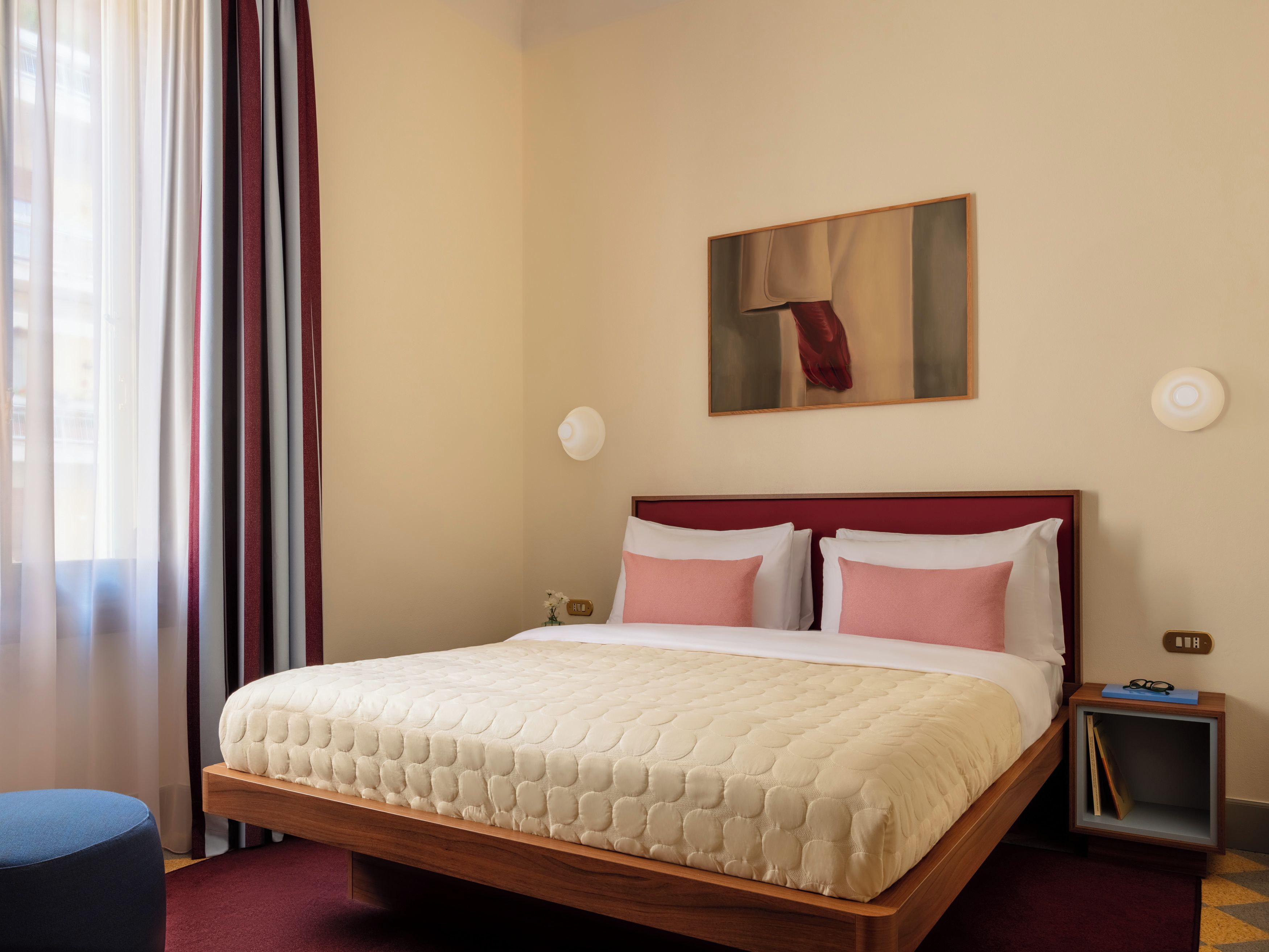 A hotel room with a bed, a nightstand, a lamp, and a painting on the wall.