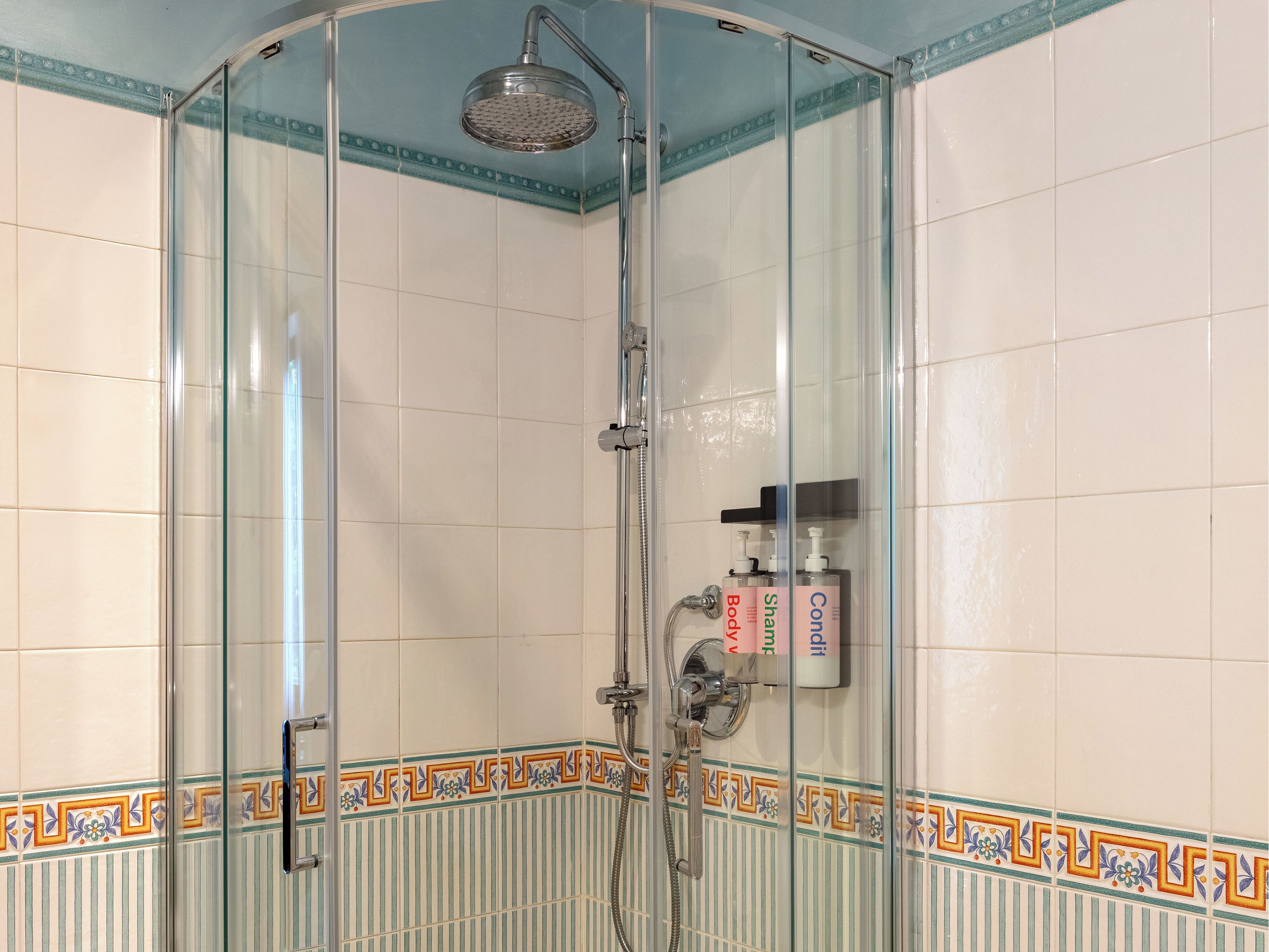Eine Duschkabine mit einer Handbrause, einem zusätzlichen Duschkopf und einer Ablage für Shampoo und Conditioner.