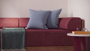 A red sofa with two pillows, a green throw blanket, and a small round table with a book and glasses. - Numa Florence della Robbia (Florence)