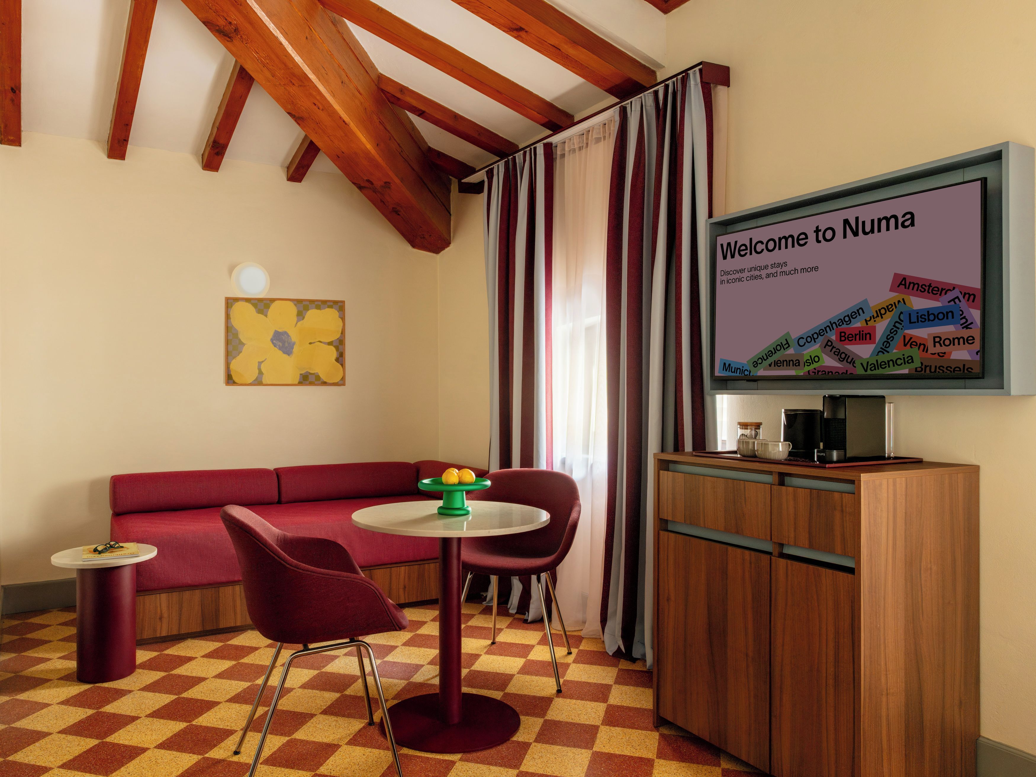 Ein modernes Zimmer mit einem roten Sofa, einem kleinen runden Tisch mit zwei Stühlen, einem Fernseher, der eine Willkommensbotschaft zeigt, und einer Holzkabine.