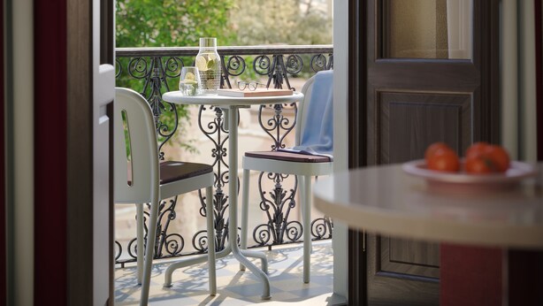 An open door leading to a balcony with a table and chairs, a small plate with tomatoes, and a view of greenery outside. - Numa Florence della Robbia (Florence)