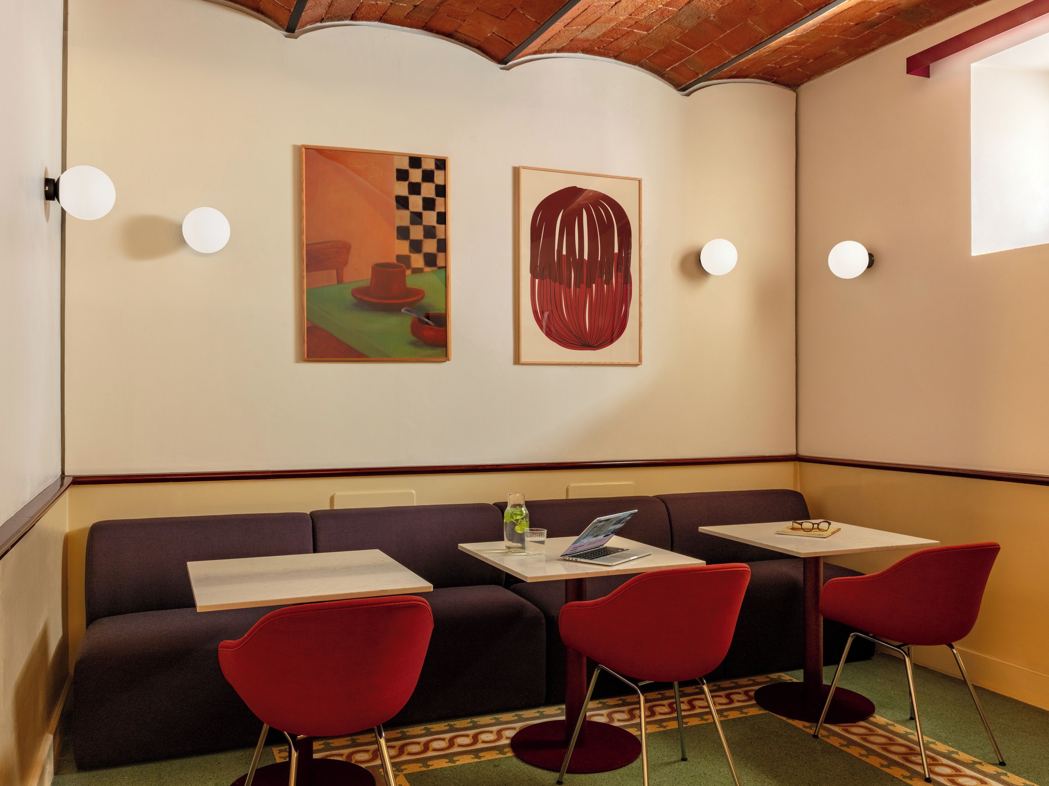 A room with a sofa, two red chairs, a table with a laptop, and two paintings on the wall.