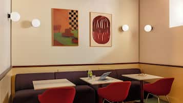 A room with a sofa, two red chairs, a table with a laptop, and two paintings on the wall.