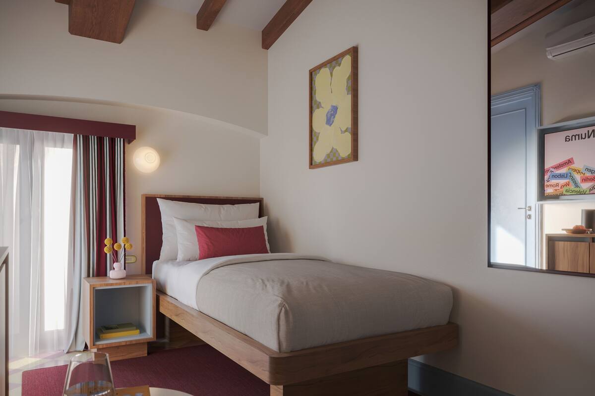 A bedroom with a bed, bedside table, lamp, and a window with curtains.