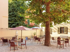 An outdoor café area with tables and chairs, surrounded by trees and buildings. - Numa Florence della Robbia (Florence)