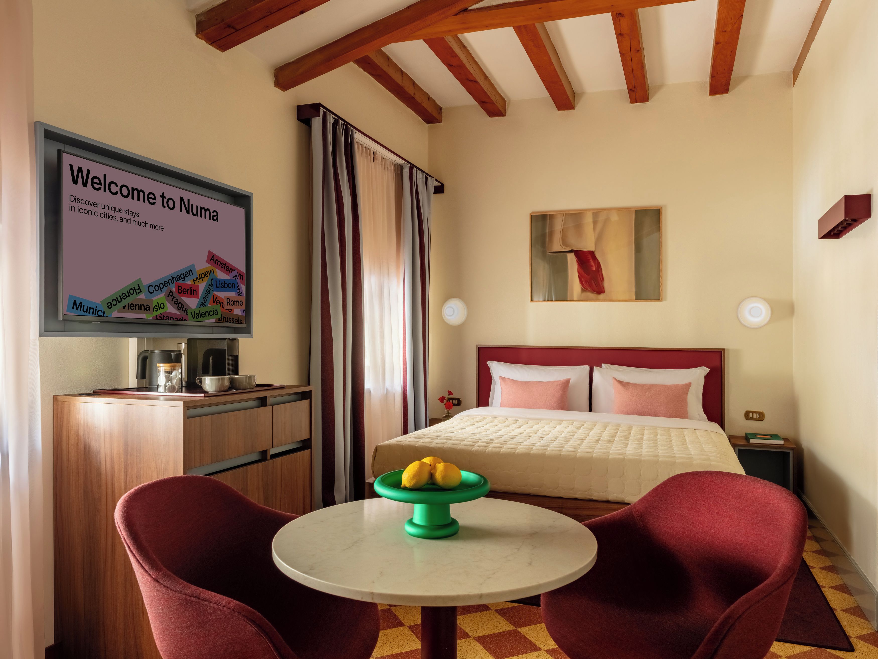 Habitación de hotel con cama, escritorio con cafetera, mesa con fruta y un cartel de bienvenida a Numata.