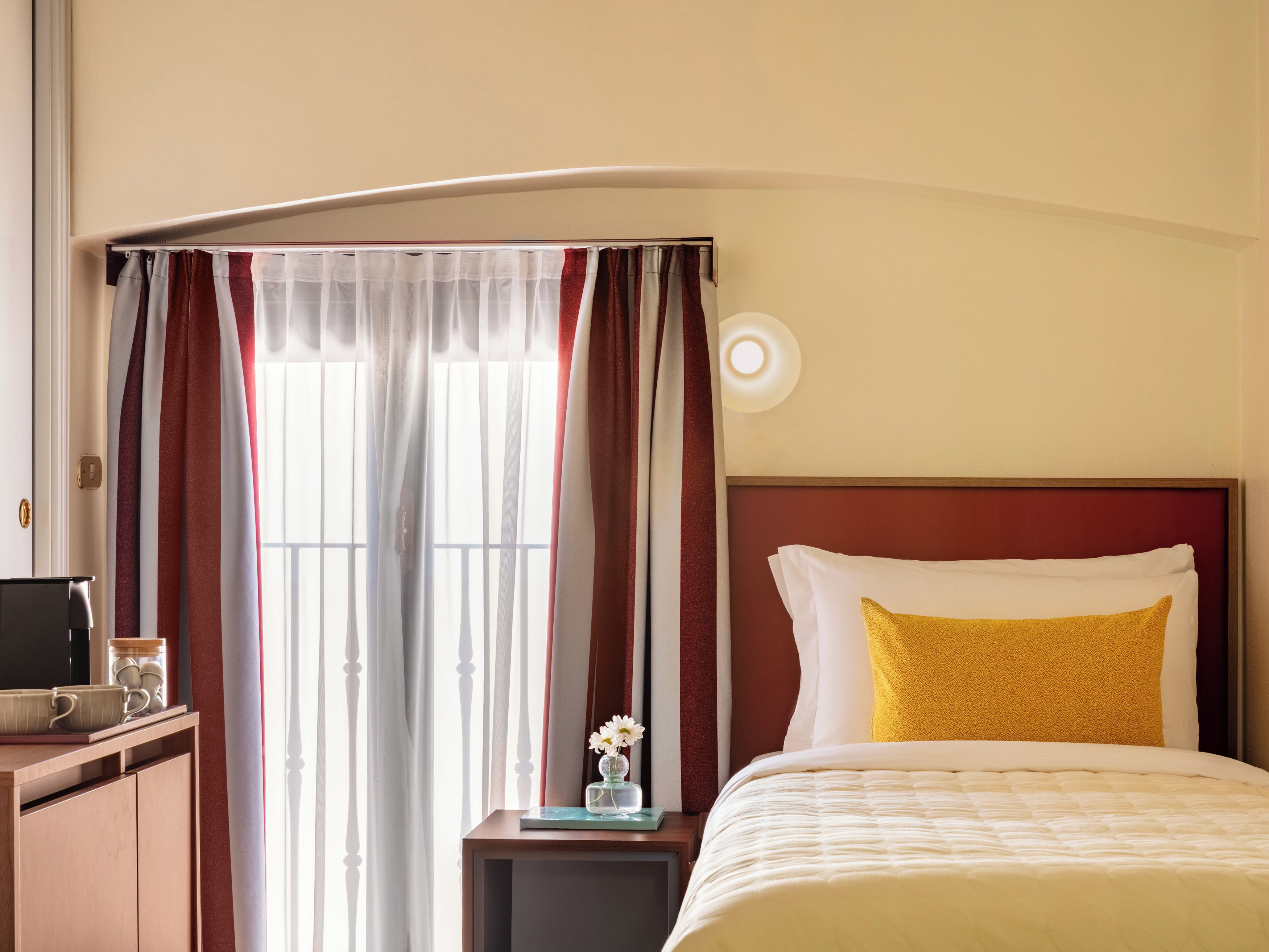 Ein Hotelzimmer mit Bett, Nachttisch, Fenster mit Vorhängen.