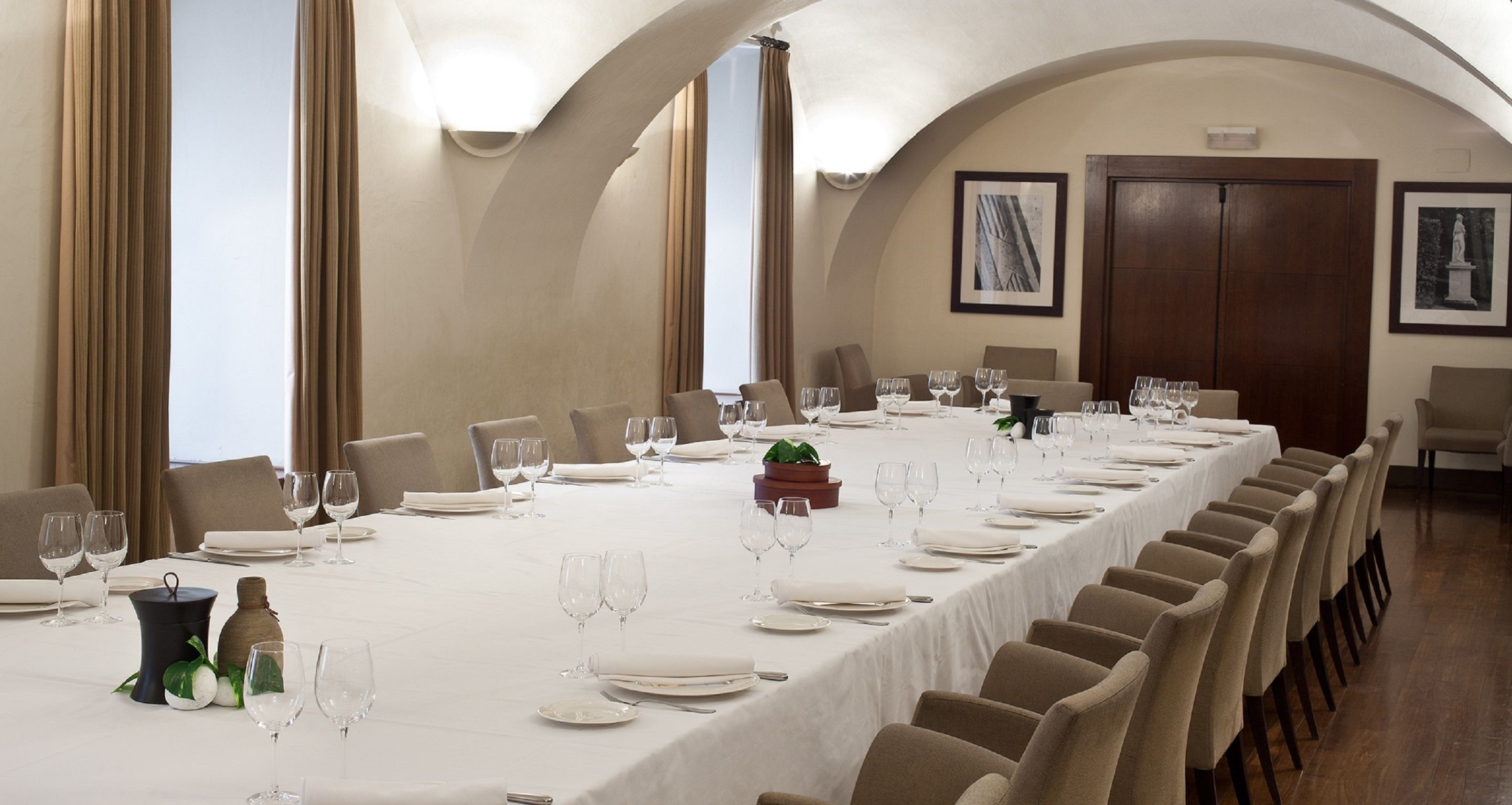 A long dining table set for a formal meal with multiple chairs, a white tablecloth, and wine glasses.