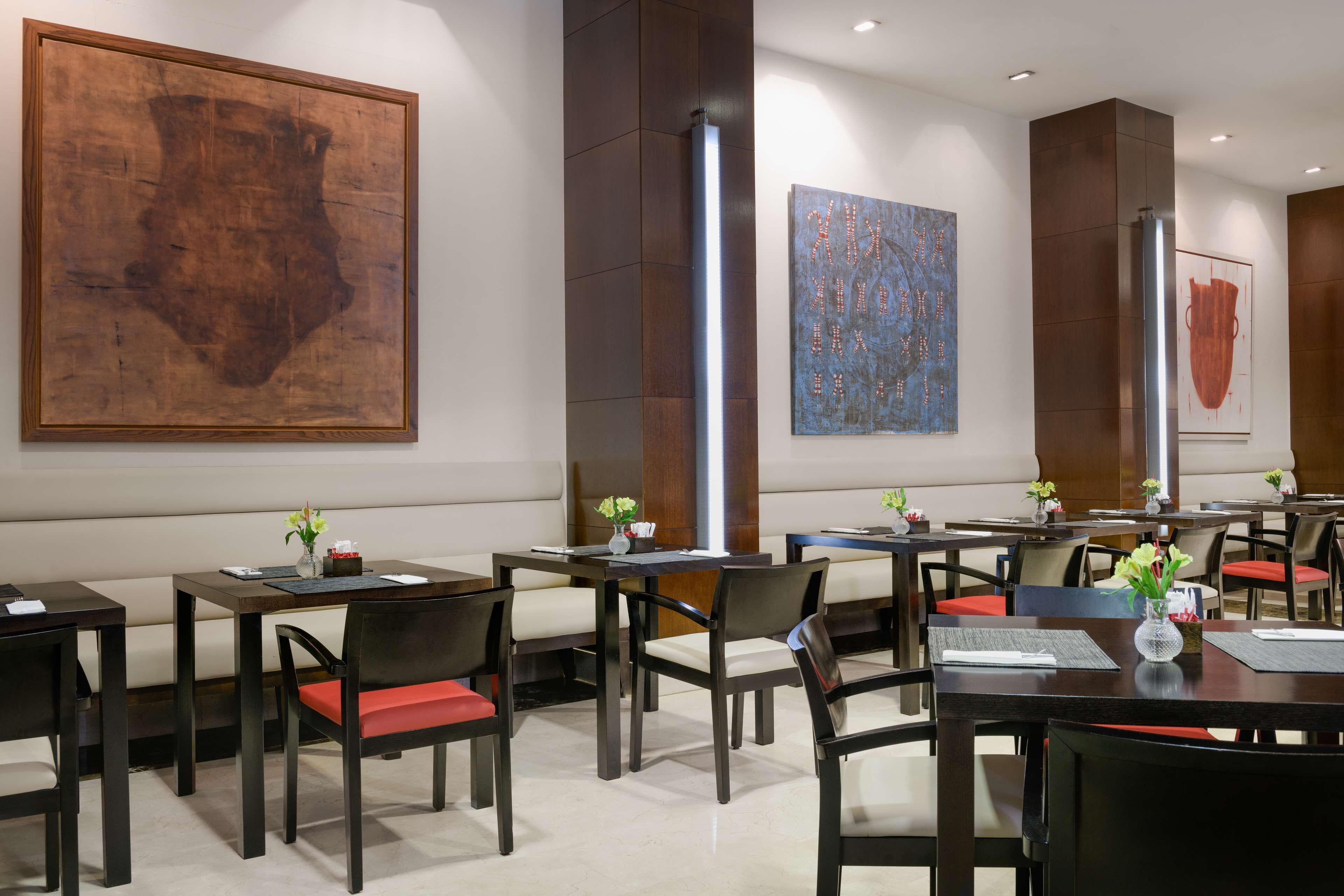 A modern restaurant with wooden tables and chairs, large abstract paintings on the walls, and a clean, minimalist design.