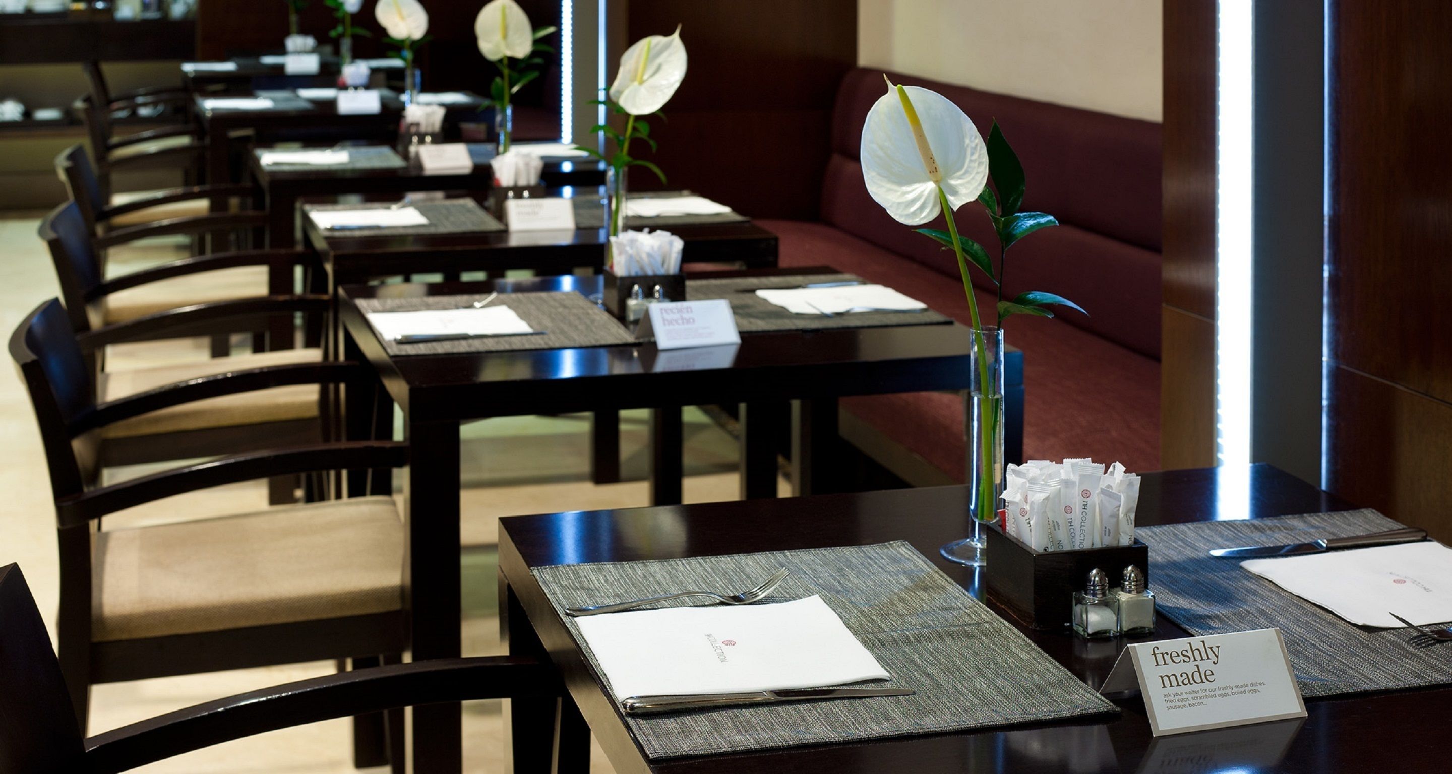 Een restaurantgedeelte van een hotel met gedekte tafels voor gasten, elk met een menukaart, een glas water en een bloevas.