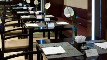 Een restaurantgedeelte van een hotel met gedekte tafels voor gasten, elk met een menukaart, een glas water en een bloevas.