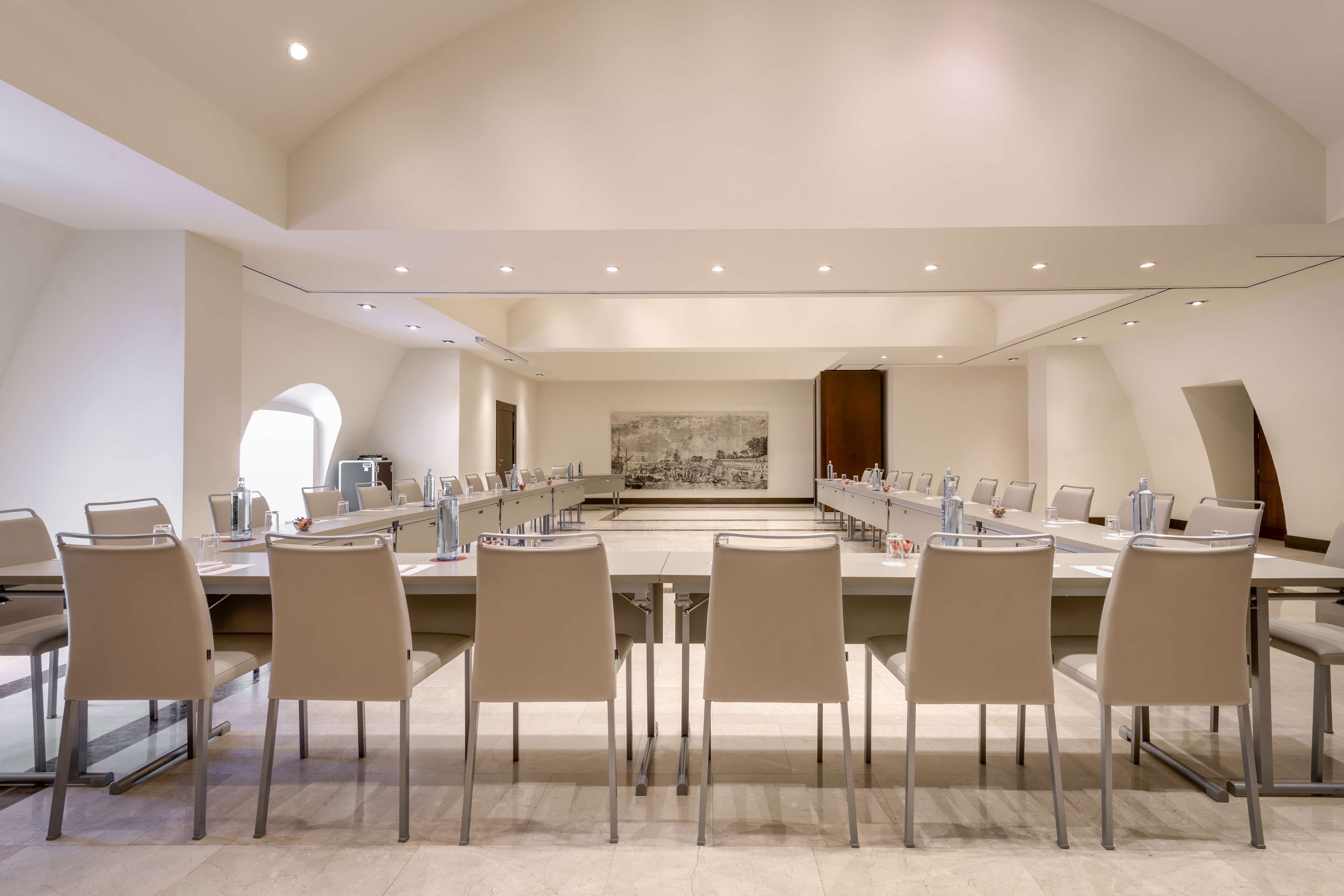 A conference room with a long table, multiple chairs, and a large painting on the wall.