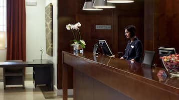 Un comptoir d’accueil avec une pancarte indiquant « DIRECTION », un vase rempli de fleurs blanches, une caisse enregistreuse et un bol de bonbons multicolores.