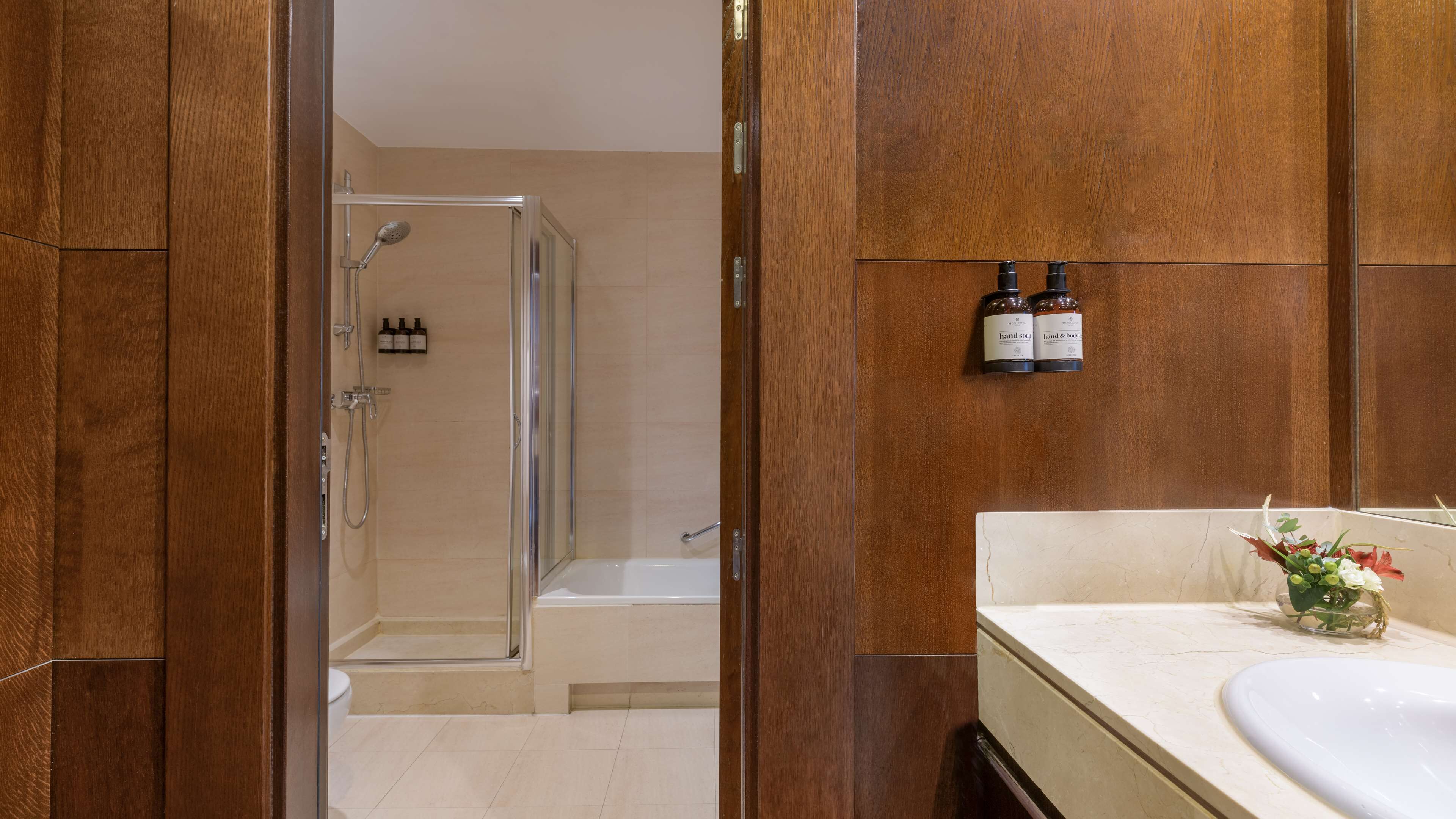 A modern bathroom with a glass-enclosed shower, a white sink, and two bottles of hand soap on the wall.