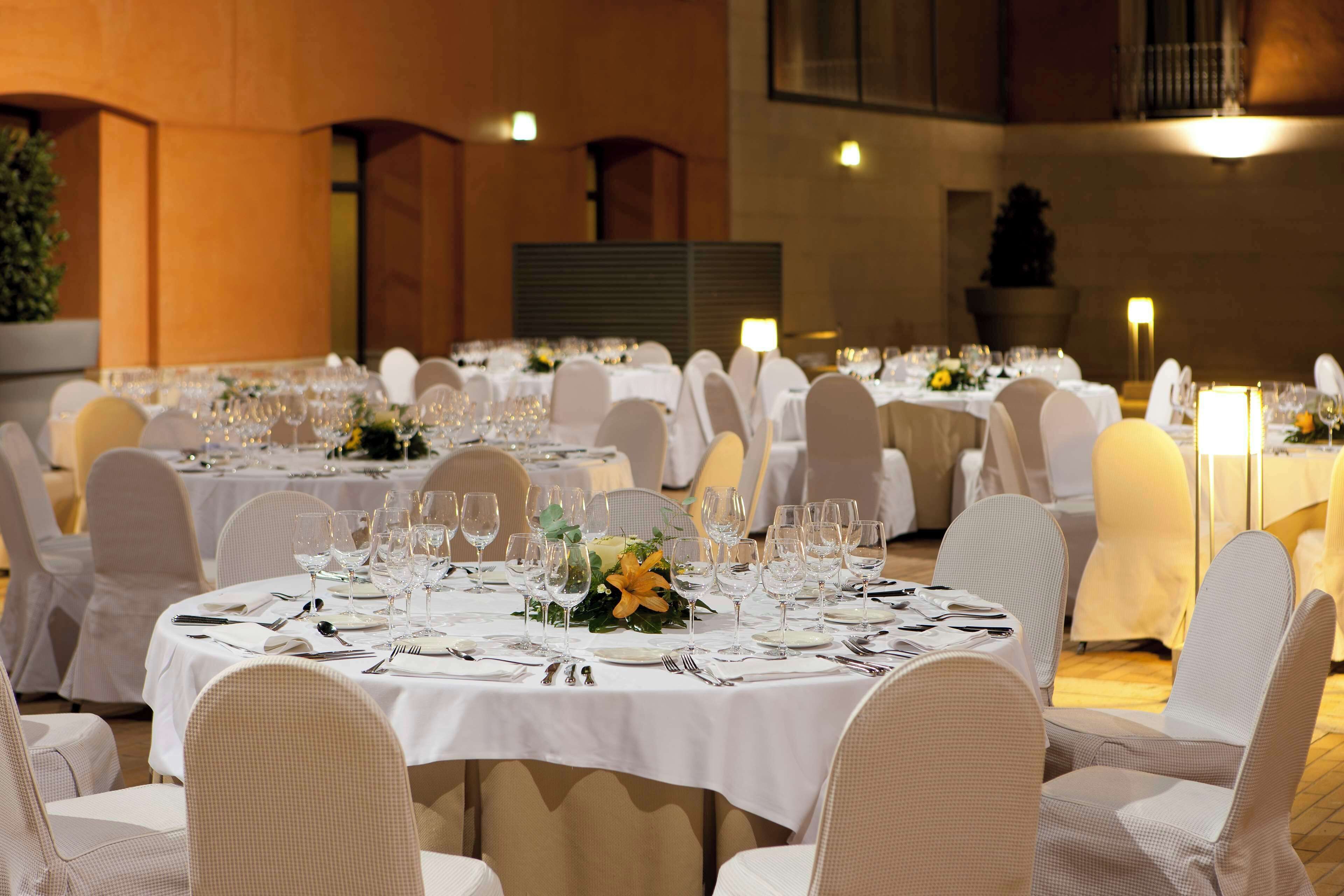 Un salón de banquetes con mesas redondas dispuestas para un evento formal, con manteles blancos, sillas y centros de mesa florales.