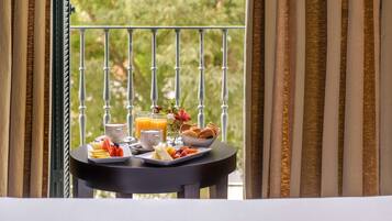 A breakfast table with a variety of food items and drinks, set against a balcony with a view of greenery.