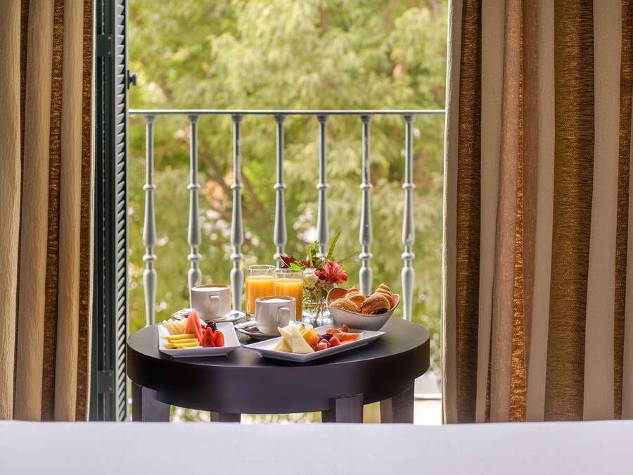 A breakfast table with a variety of food items and drinks, set against a balcony with a view of greenery.