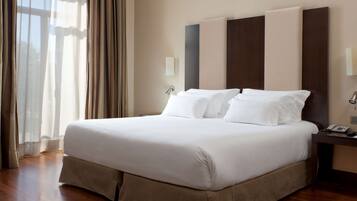 Camera d'albergo con un letto grande, pavimento in legno, un comodino con un telefono e una finestra con tende.