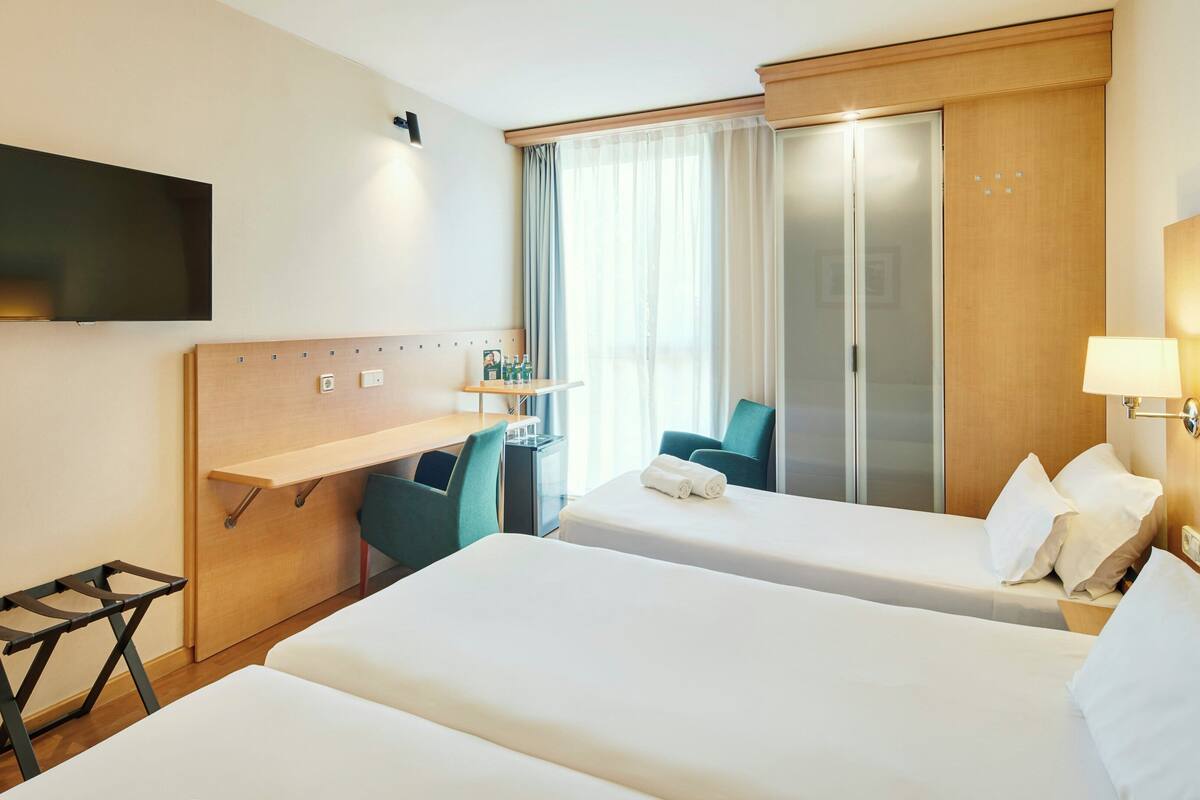 A hotel room with two beds, a desk, a TV, and a wardrobe.