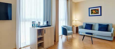 Una sala de estar moderna con sofá, una mesa de centro, televisor, escritorio con lámpara y un amplio ventanal con cortinas.