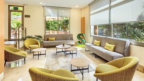 A modern lobby with a sofa, chairs, a coffee table, and a large letter 'S' decoration. - Sercotel Porta Barcelona (Sant Just Desvern)
