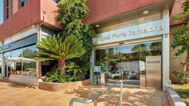 A hotel entrance with a palm tree, a sign for 'Sercotel Porta Barcelona,' and a visible car in the parking area. - Sercotel Porta Barcelona (Sant Just Desvern)