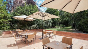 An outdoor patio area with tables and chairs, surrounded by greenery and trees. - Sercotel Porta Barcelona (Sant Just Desvern)