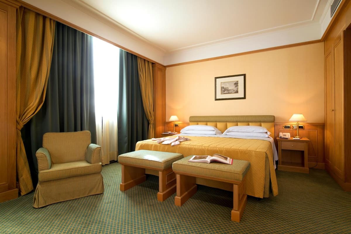 A hotel room with a bed, a chair, two nightstands, and a window with curtains.