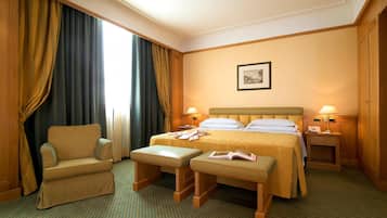 Una habitación de hotel con cama, una silla, dos mesitas de noche y una ventana con cortinas.