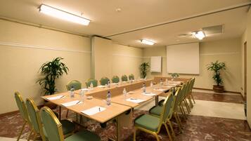 Une salle de conférence avec une longue table, des chaises, des bouteilles d’eau et un tableau blanc.