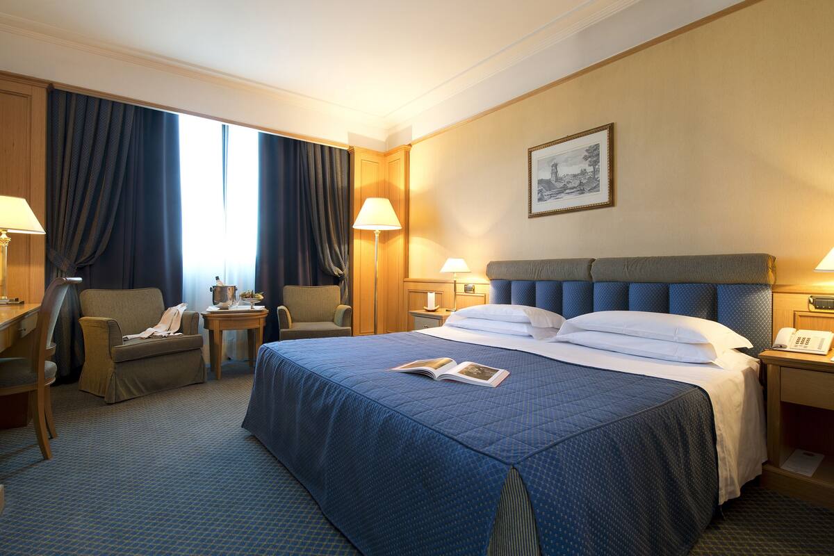A hotel room with a large bed, two chairs, a desk, and a nightstand with lamps.