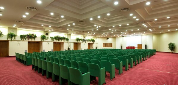 A conference room with rows of green chairs, a red carpet, and ceiling lights.
