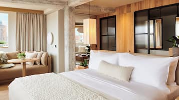 A modern hotel room with a large bed, a sofa, a small table with a plant, and a view of the city.