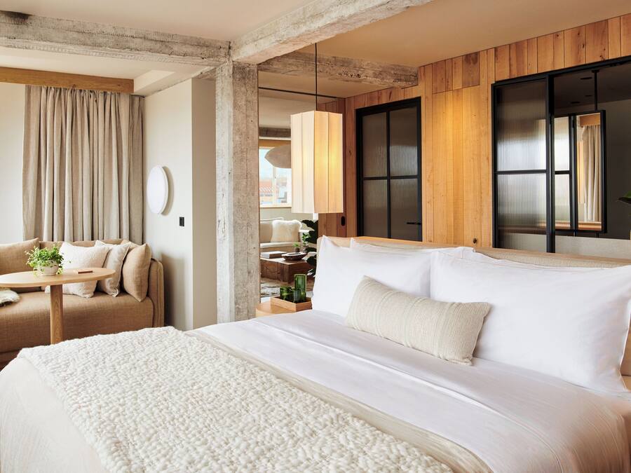 Een moderne hotelkamer met een groot bed, een bank, een klein tafeltje met een plant en uitzicht op de stad.