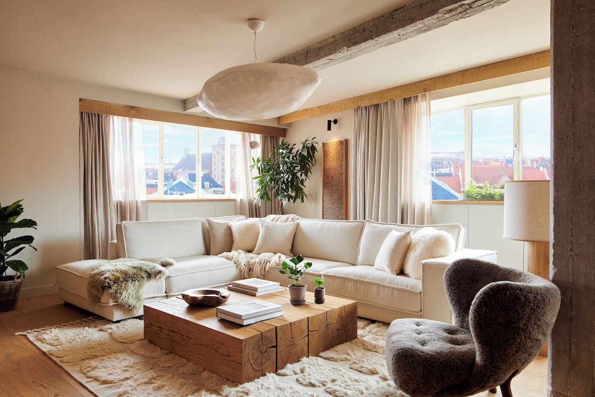 A modern living room with a sectional sofa, a wooden coffee table, a potted plant, and a view of the city through large windows.