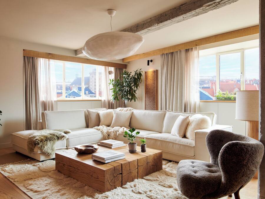 A modern living room with a sectional sofa, a wooden coffee table, a potted plant, and a view of the city through large windows.