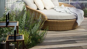 A wicker sofa with cushions on a wooden deck, overlooking a cityscape with buildings and a tower. - 1 Hotel Copenhagen (Copenhagen)
