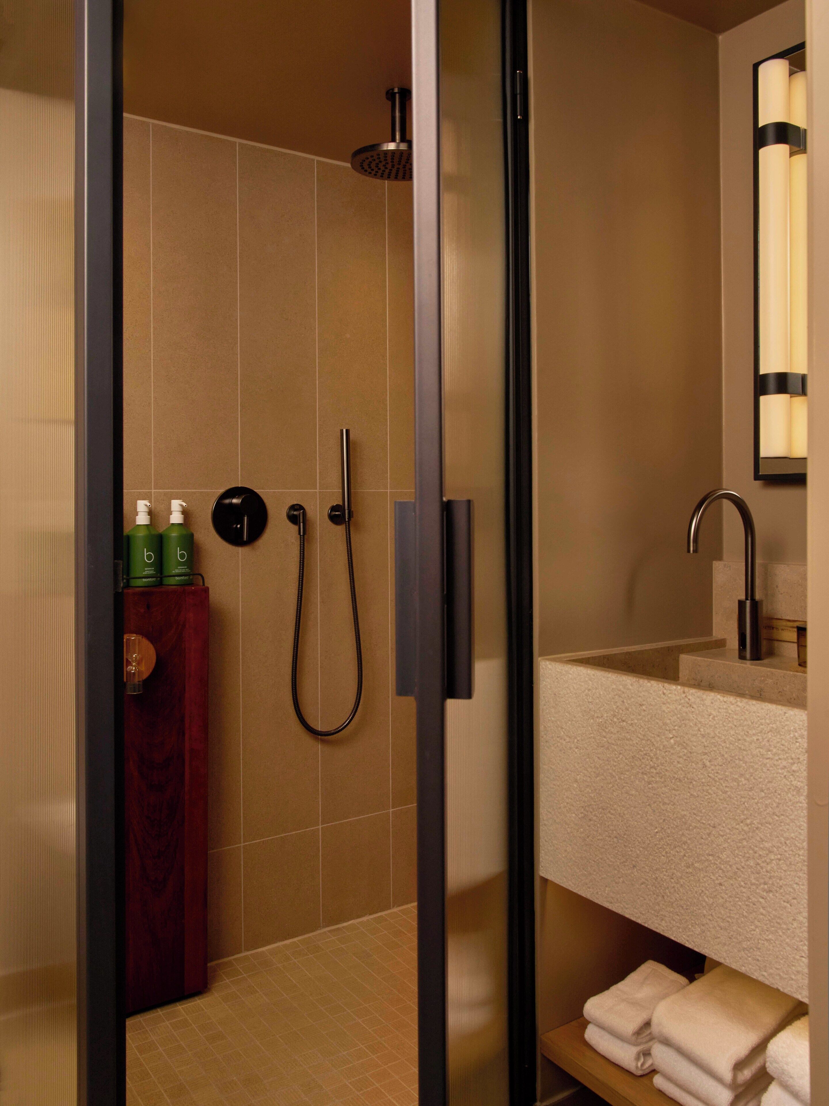A modern bathroom with a glass-enclosed shower, a wooden cabinet with toiletries, and a sink with a mirror.