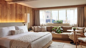 A modern hotel room with a large bed, a sofa, a small table, and a view of a cityscape through large windows. - 1 Hotel Copenhagen (Copenhagen)