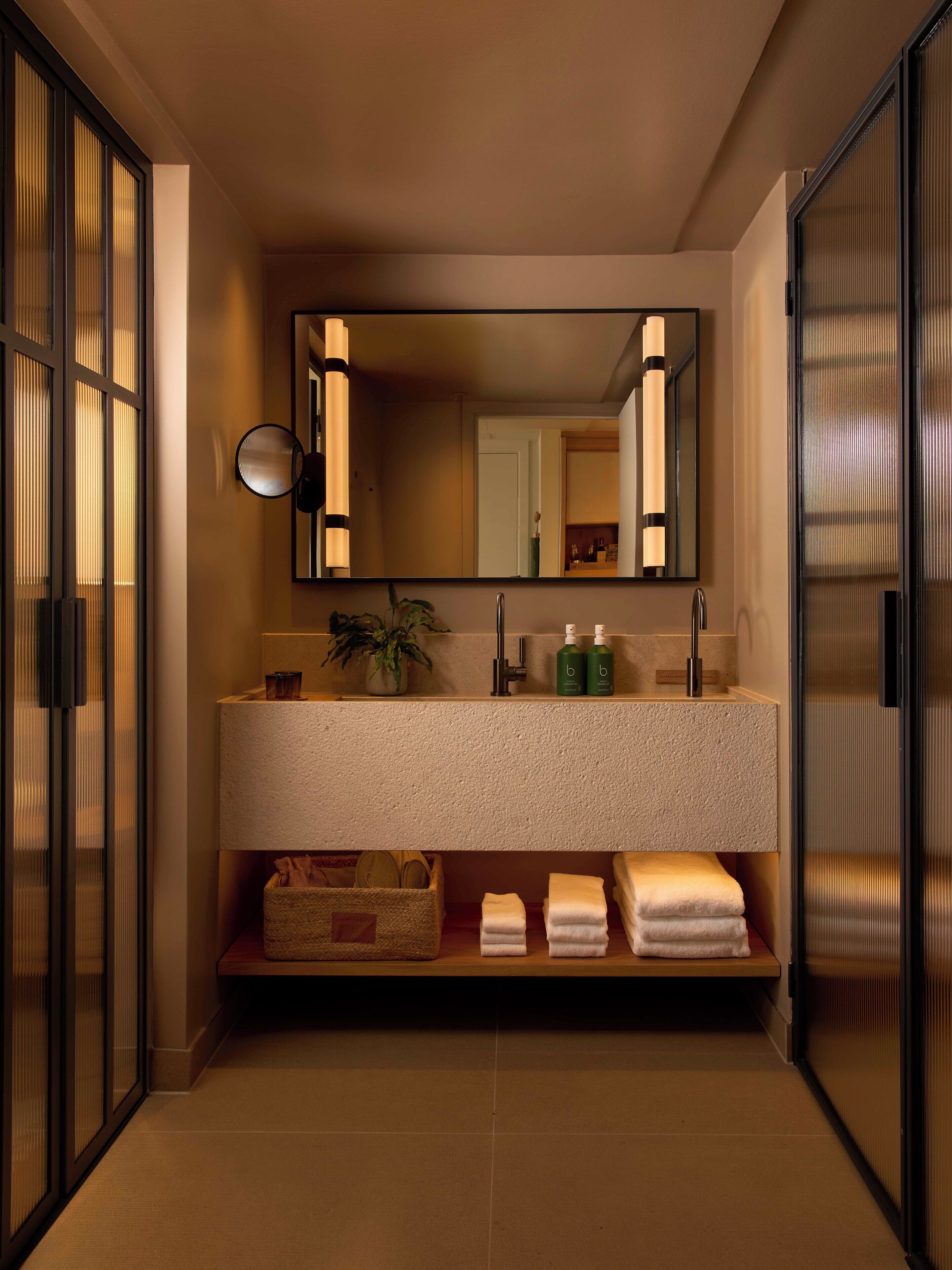 A modern bathroom with a large mirror, a sink with toiletries, and a towel rack.