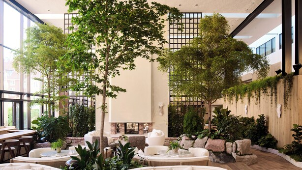 A spacious indoor area with multiple seating arrangements, including sofas and chairs, surrounded by various plants and a large tree. - 1 Hotel Copenhagen (Copenhagen)