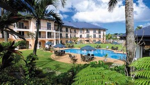 A hotel with a swimming pool, outdoor seating, and lush greenery. - Tradewinds Hotel (Ottoville)