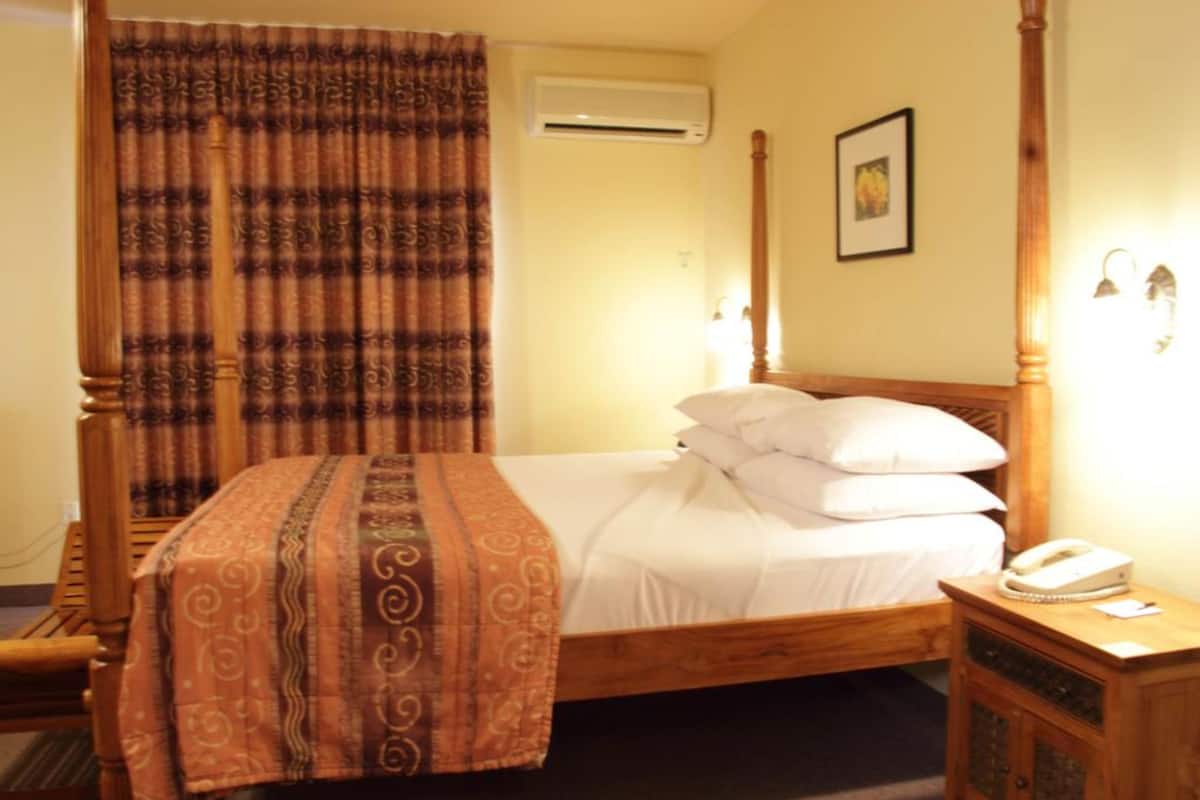 A hotel room with a wooden bed, a bedside telephone, and a curtain.