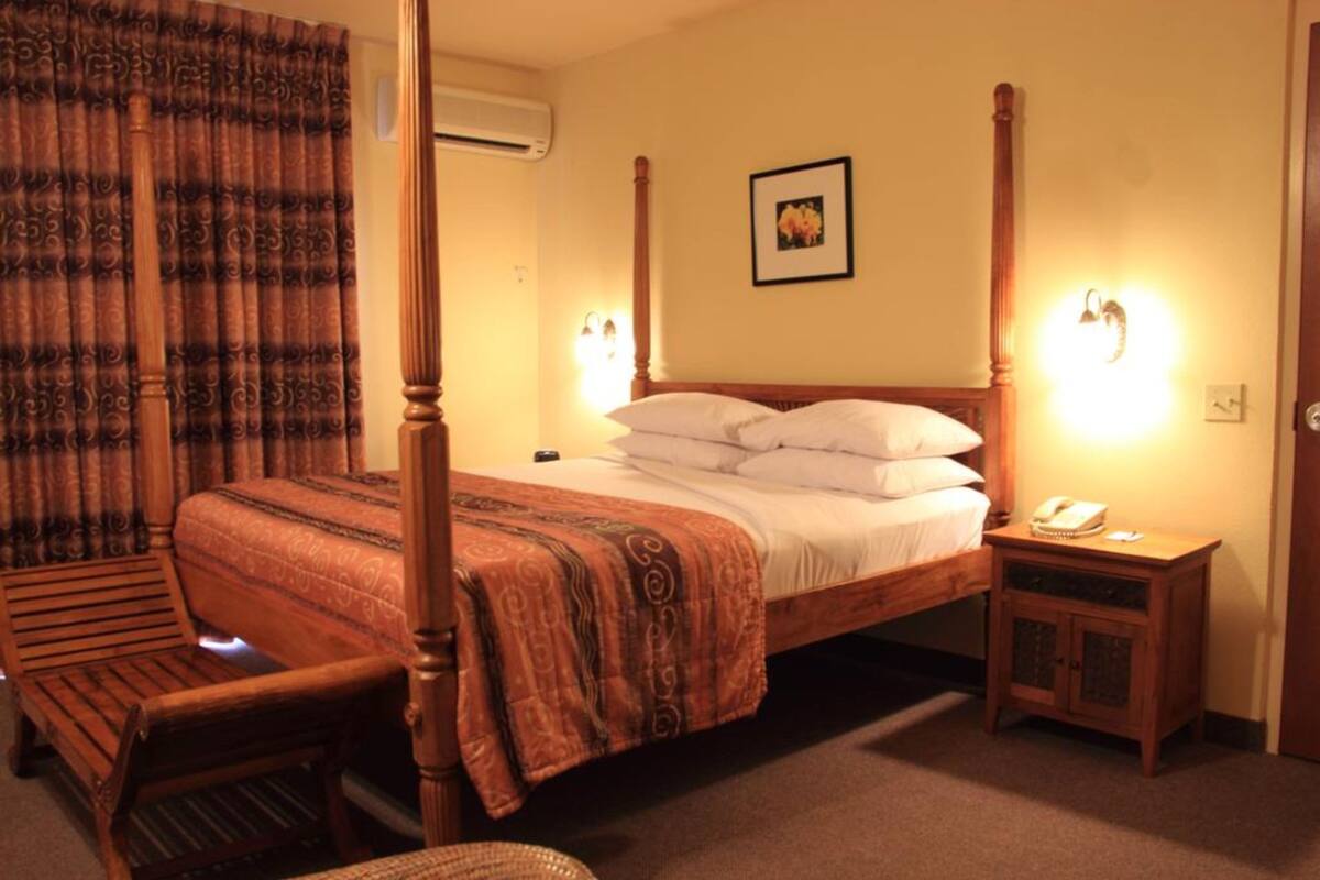 A four-poster bed with a patterned bedspread, a bedside table with a lamp, and a chair.