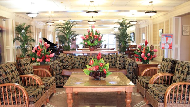 A lobby with a central coffee table, floral arrangements, and patterned sofas. - Tradewinds Hotel (Ottoville)