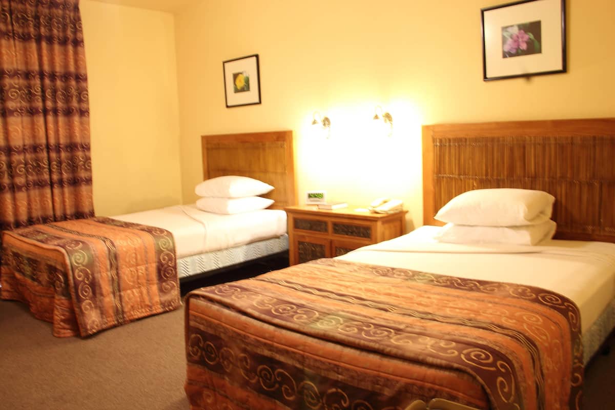 A hotel room with two single beds, a wooden headboard, a nightstand with a lamp, and a framed picture on the wall.