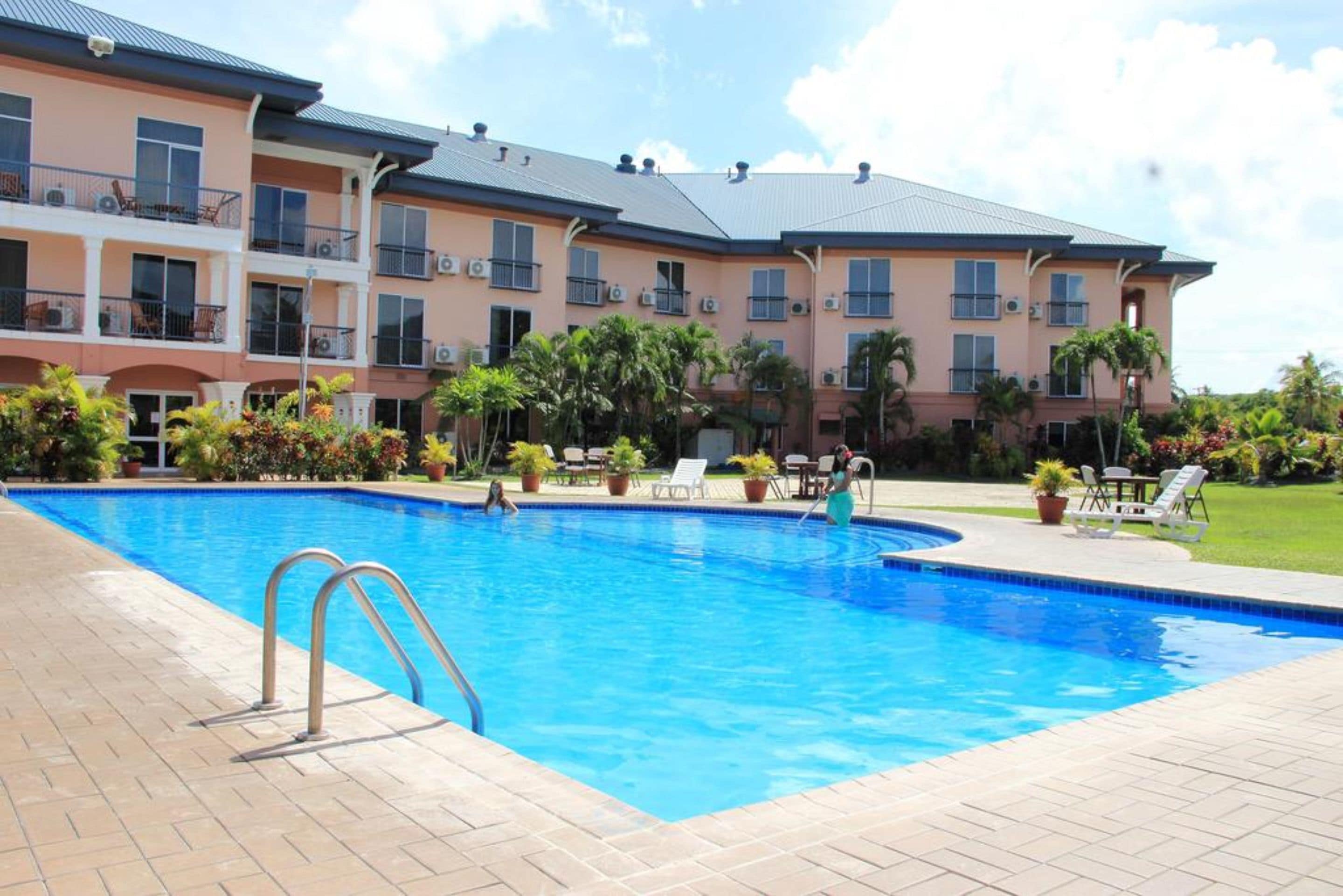 A swimming pool with a clear blue water, surrounded by a brick patio. There are lounge chairs and potted plants around the pool.