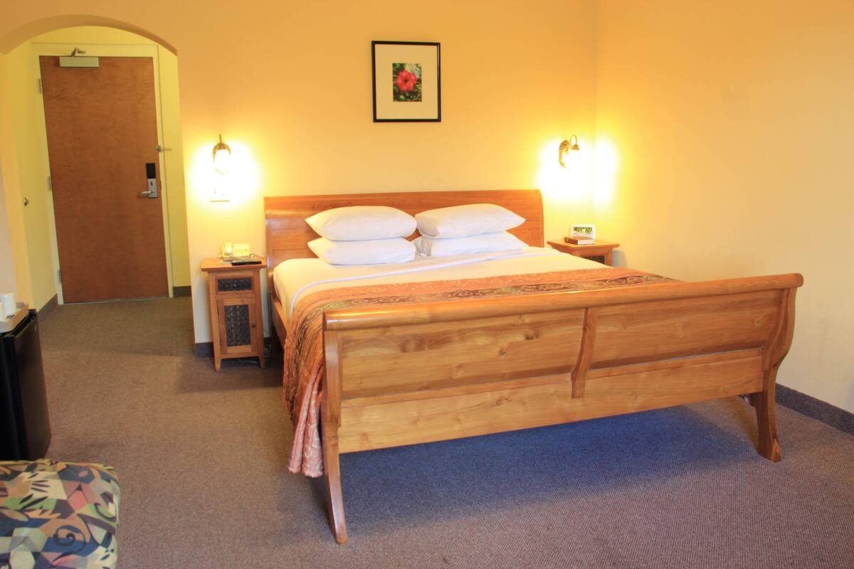 A hotel room with a wooden bed, two bedside tables, a nightstand, a small cabinet, and a framed picture on the wall.