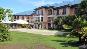 A multi-story hotel with balconies, a courtyard with outdoor seating, and lush greenery. - Tradewinds Hotel (Ottoville)
